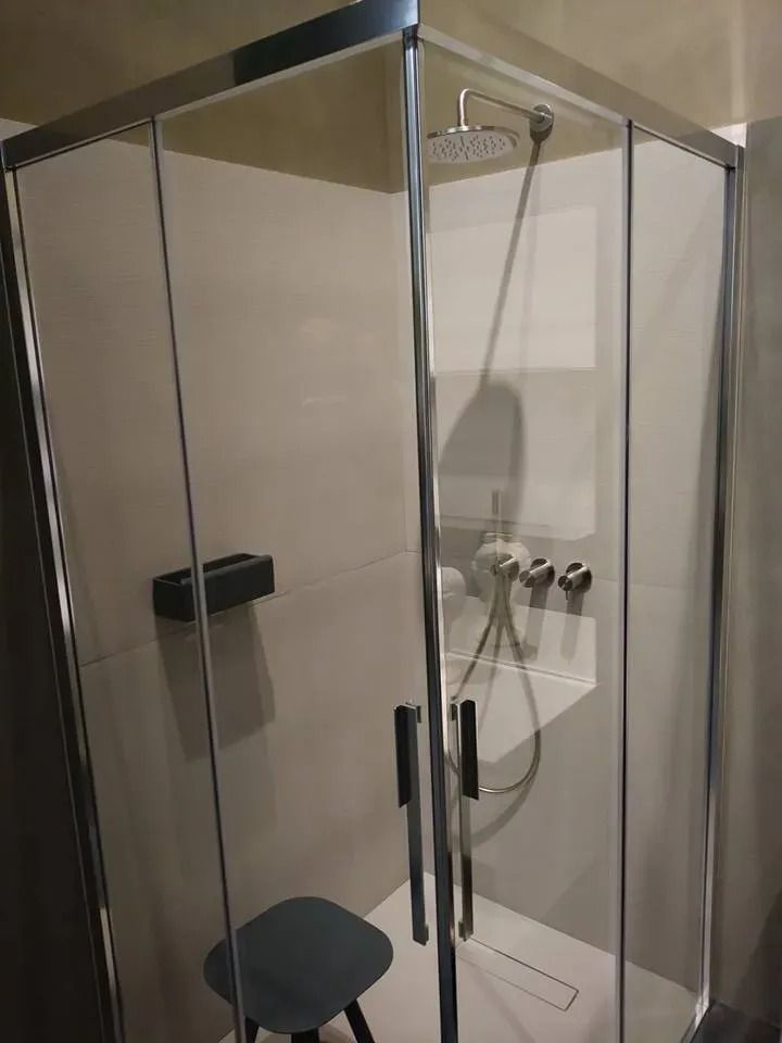 Box doccia in vetro con rubinetteria cromata e piccolo sedile nero in un bagno