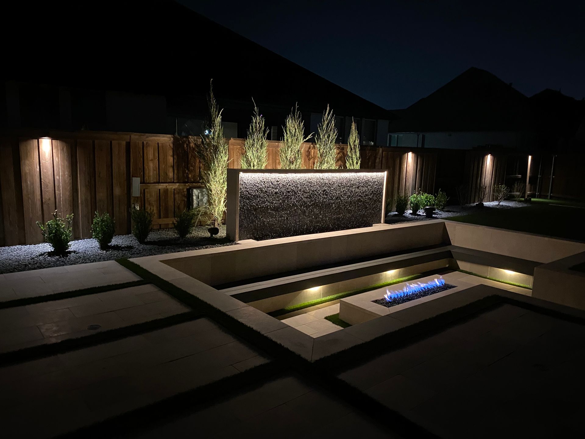 A backyard with a waterfall and a fire pit at night.