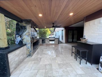 A large patio with a wooden ceiling and a grill.