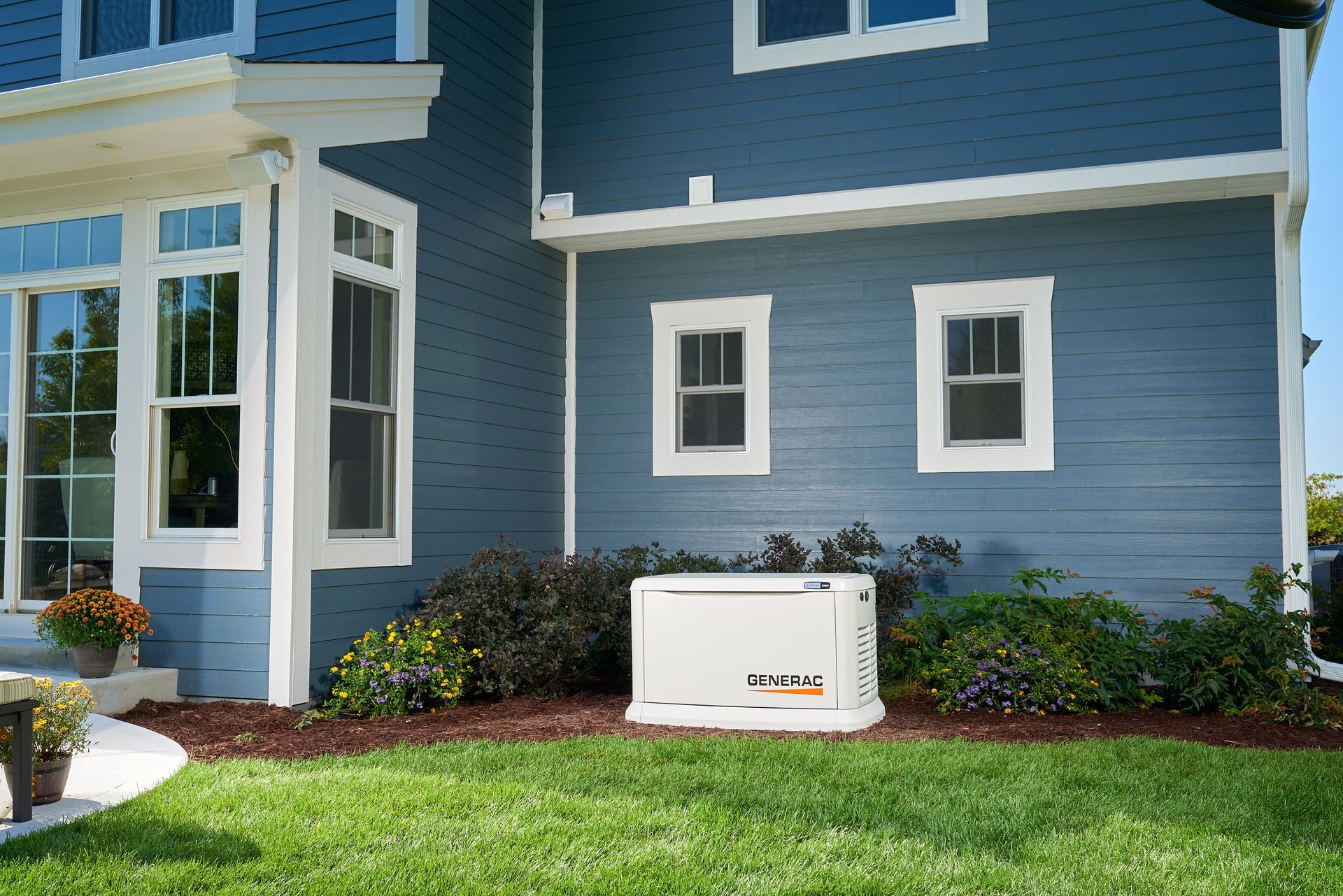 A white generator sits on a green lawn near a blue house with white trim and windows.