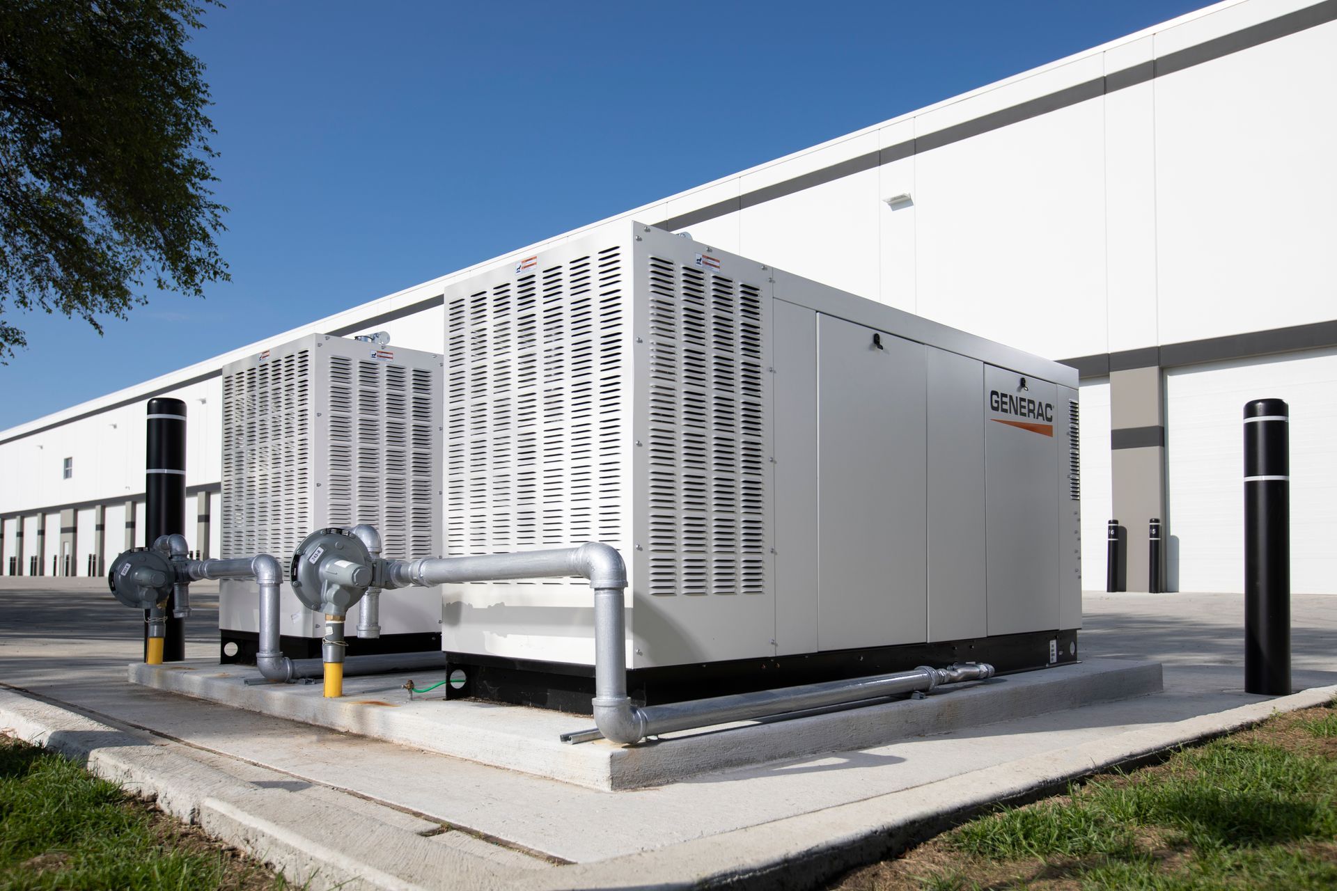 Two large, white industrial generators outside a building. They are on a concrete pad with pipes and venting visible.