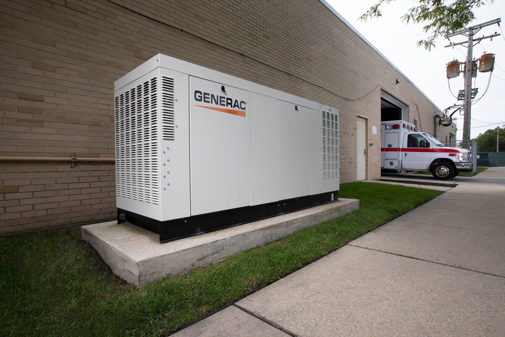 A Generac generator outside a brick building, next to an ambulance. The unit is white with the logo.