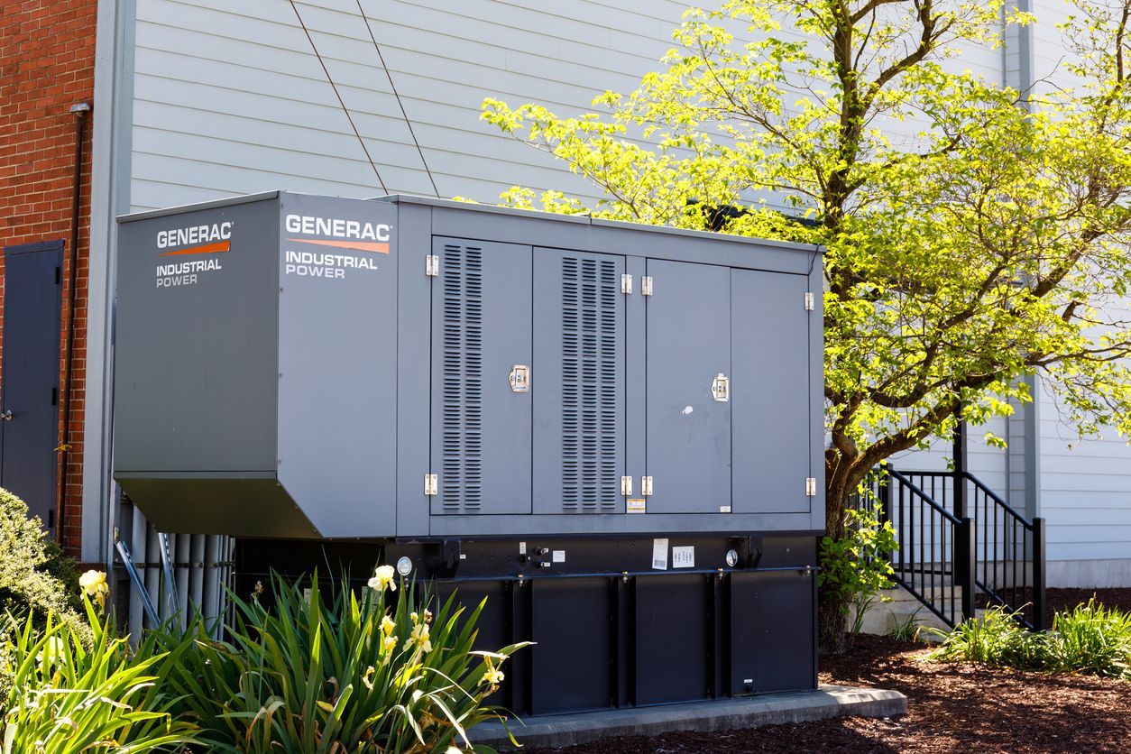 Gray Generac generator outside a building next to a tree and steps.