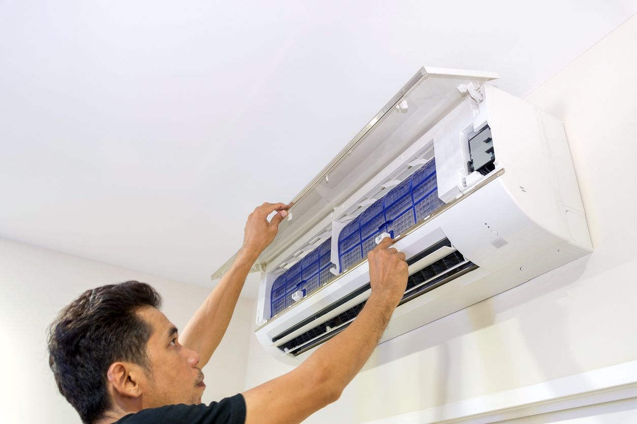 Man cleaning an air conditioner filter on a white wall, opening the unit to reveal the filters.