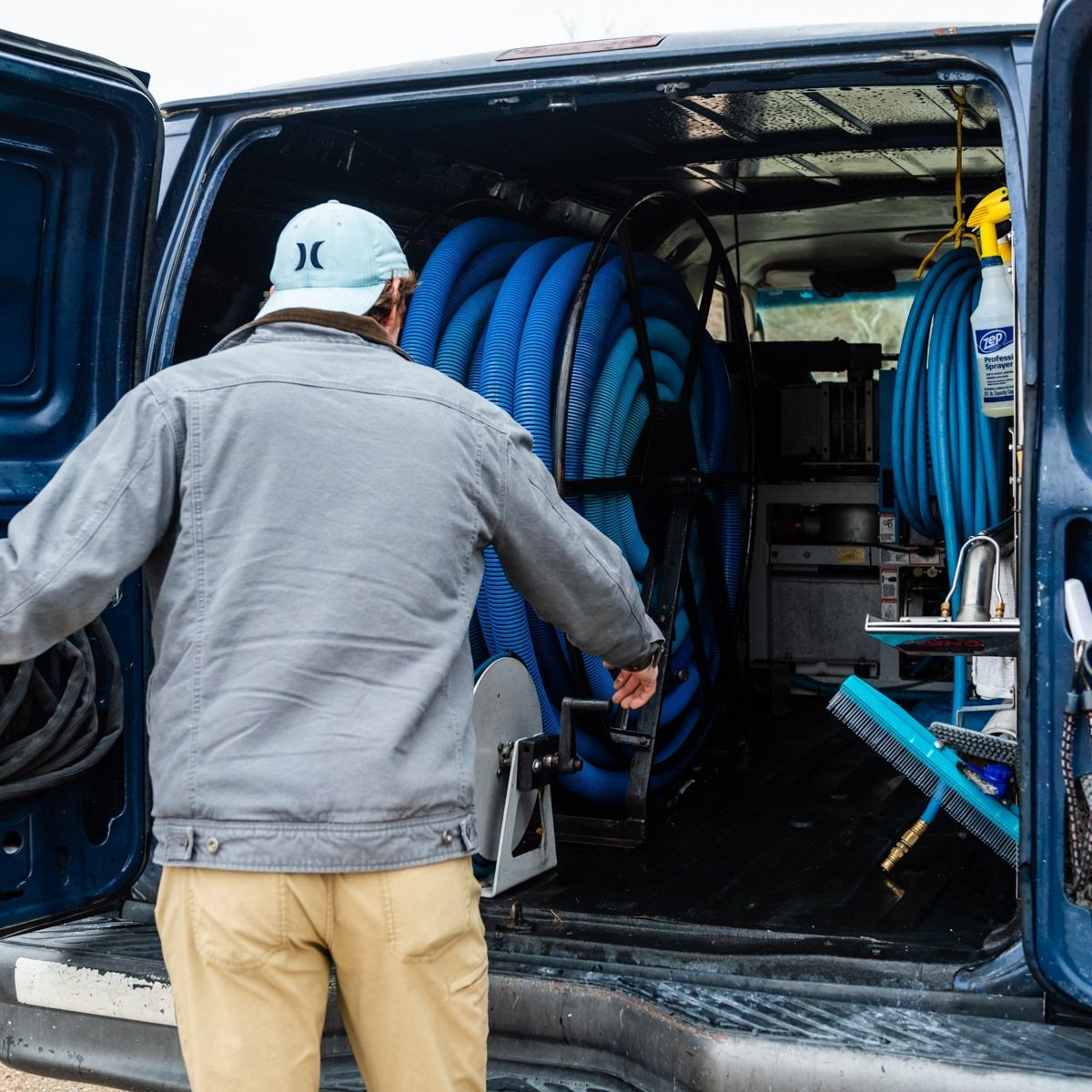 a man wearing a hurley hat is loading hose into a van