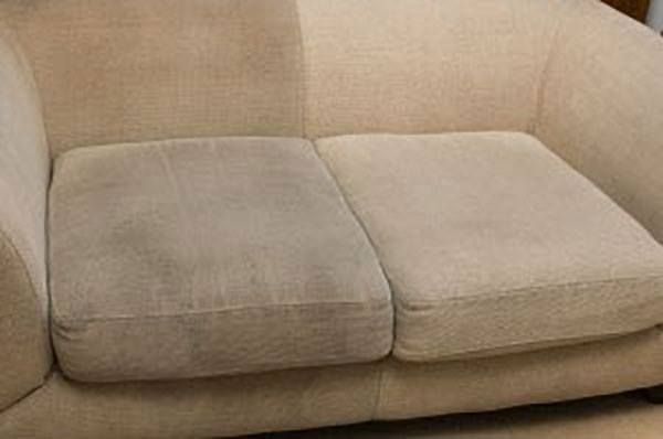 a beige couch with a dirty cushion is sitting on the floor .