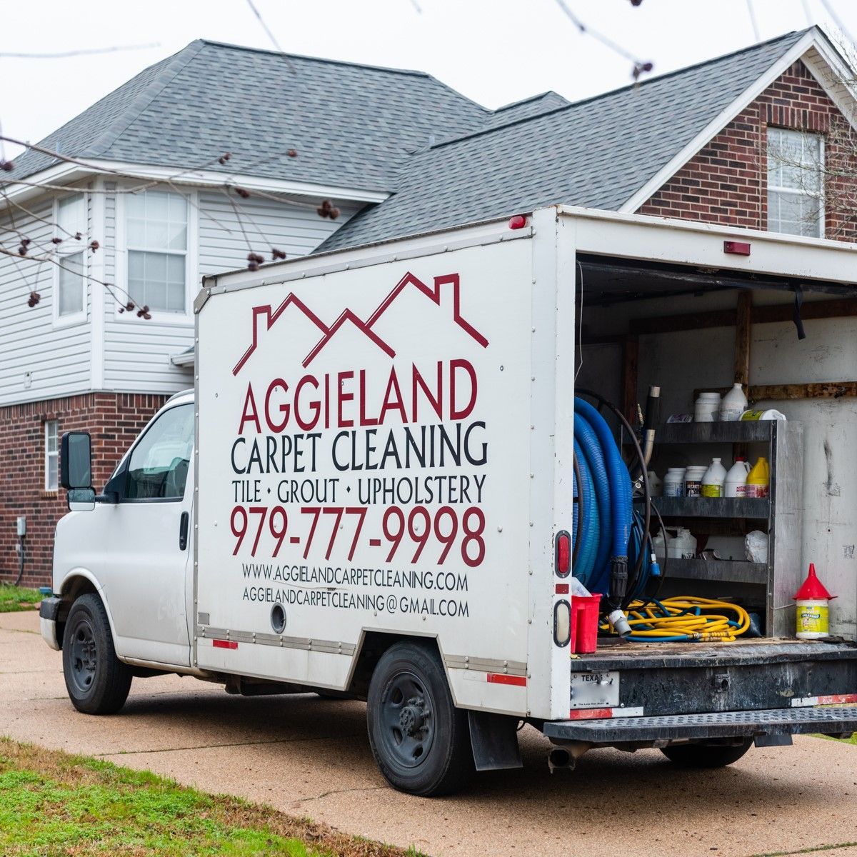 a white carpet cleaning truck is parked in front of a brick house .