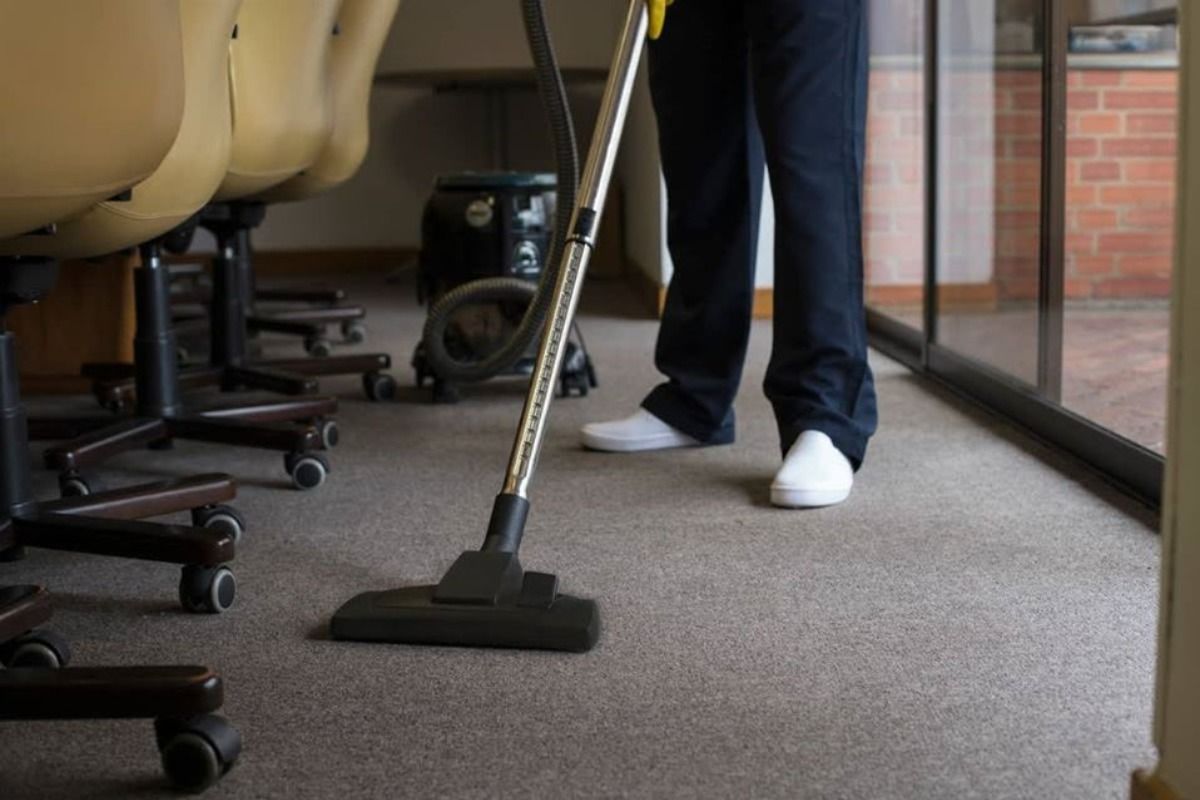 a person is using a vacuum cleaner to clean a carpet in an office .