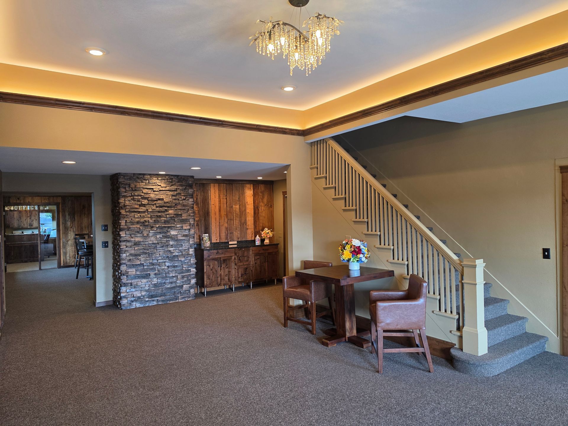 Spacious living room with staircase, chandelier, dining table, stone accent wall, and carpeted floor.