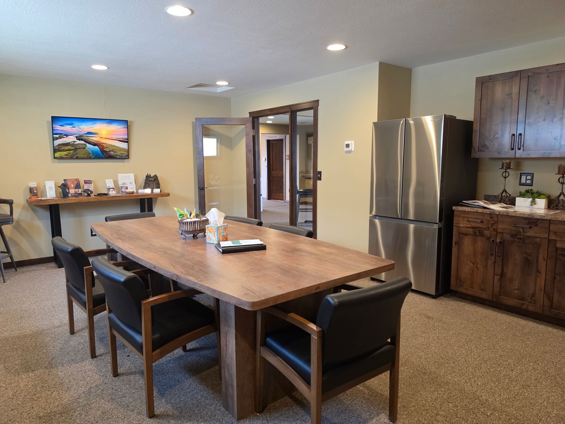 Modern kitchen and dining area with a wooden table, black chairs, stainless fridge, and wall art.