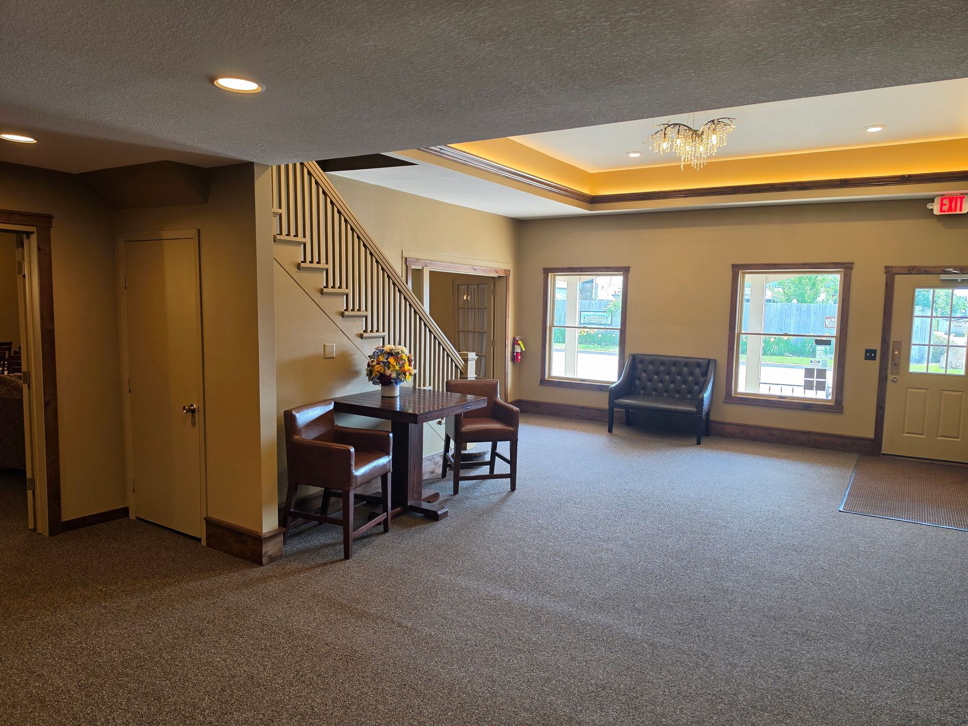 Spacious beige living room with staircase, carpeted floor, and large windows letting in daylight