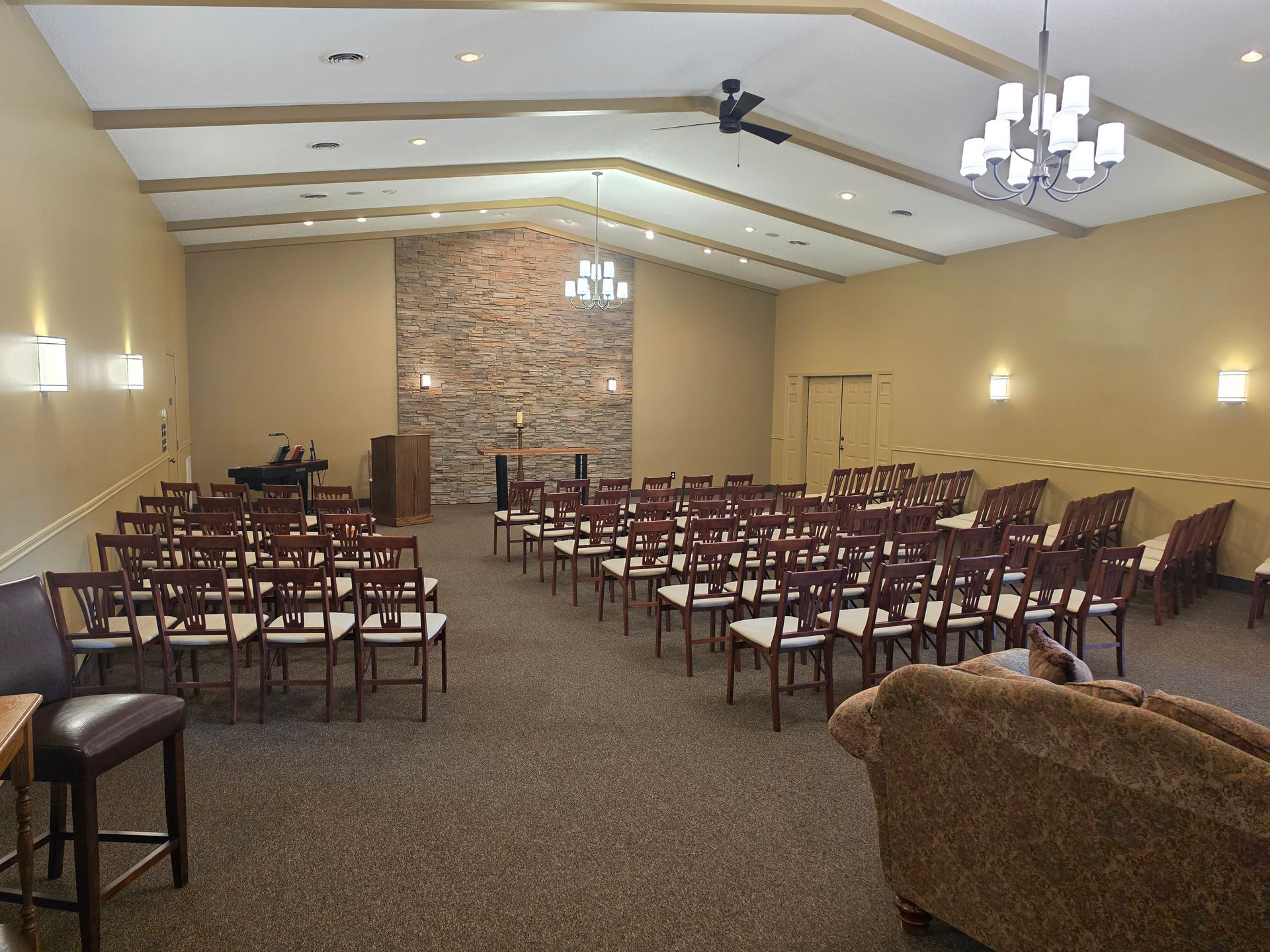 Empty banquet hall with rows of chairs, stone fireplace, beige walls, and hanging chandeliers.