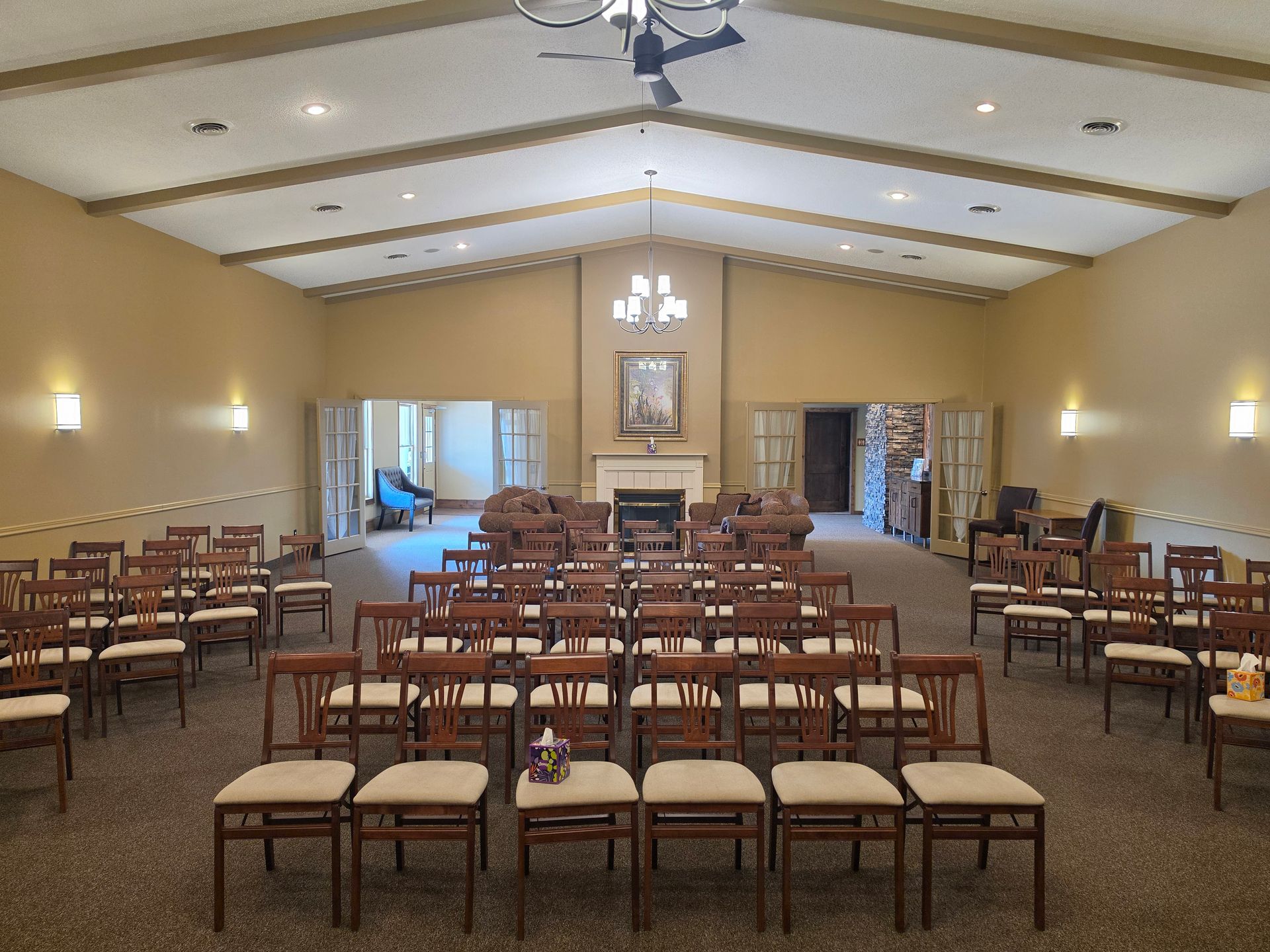 Empty banquet hall with rows of chairs and tables facing a central aisle and fireplace