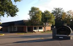 Low brick school building with trees and a sign along a quiet street