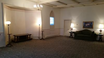 Spacious living room with white walls, carpet, sofa, table, lamps, and a chandelier
