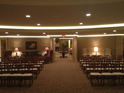 Conference hall with rows of chairs, carpeted aisle, and warm overhead lighting leading to a stage.