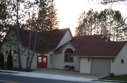 Suburban house at dusk with red double doors, garage, and trees in the background