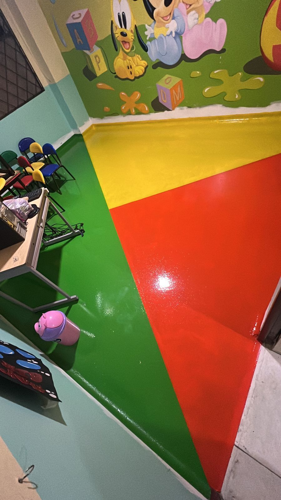 Habitación infantil con suelo pintado de verde, amarillo y rojo. Mural de personajes de dibujos animados en la pared.