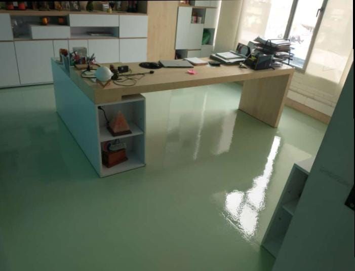 Oficina con suelo de color verde claro, escritorio grande de madera, estanterías y ventana. Pisos epóxicos