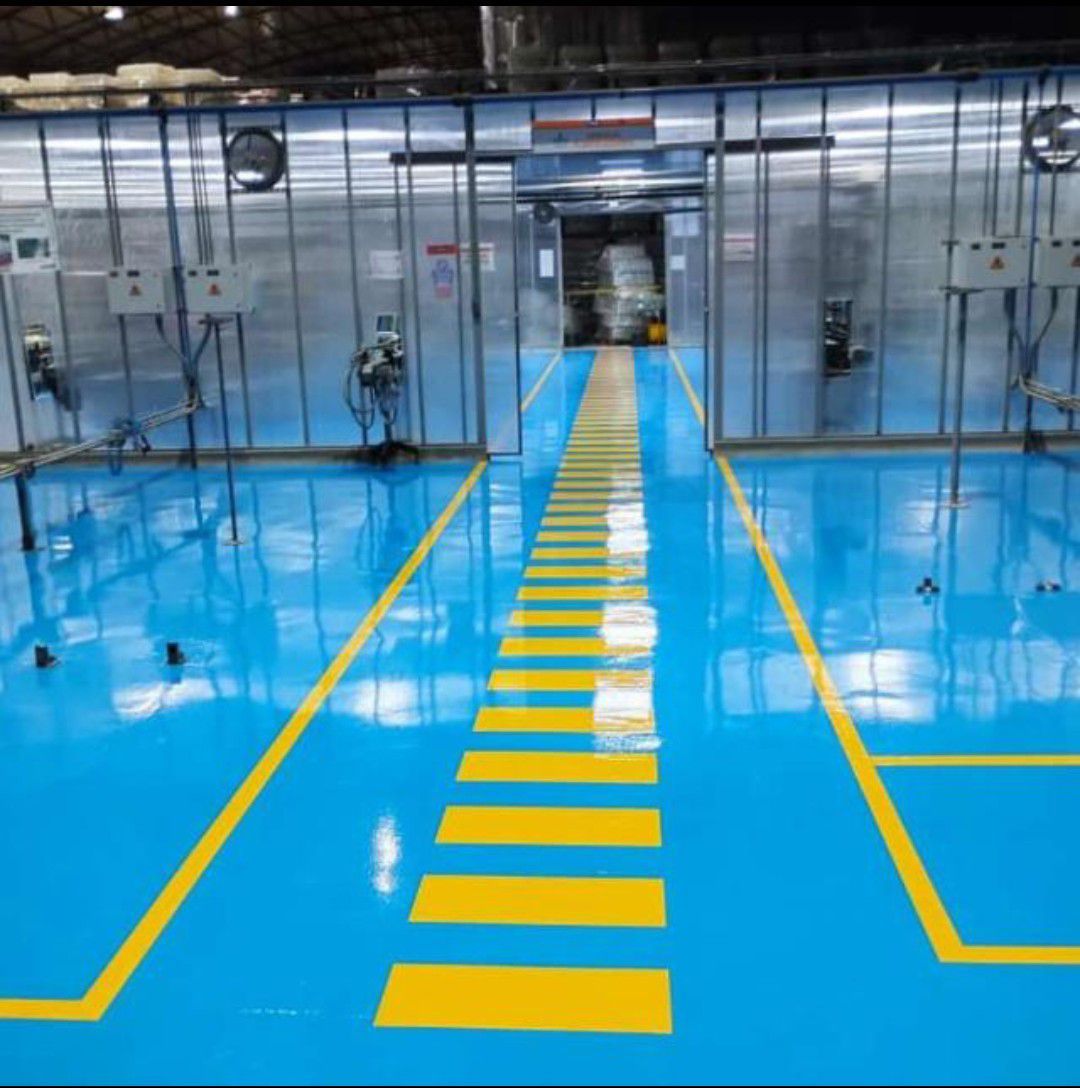 Suelo industrial azul con líneas amarillas, dos naves con equipos y una puerta central.