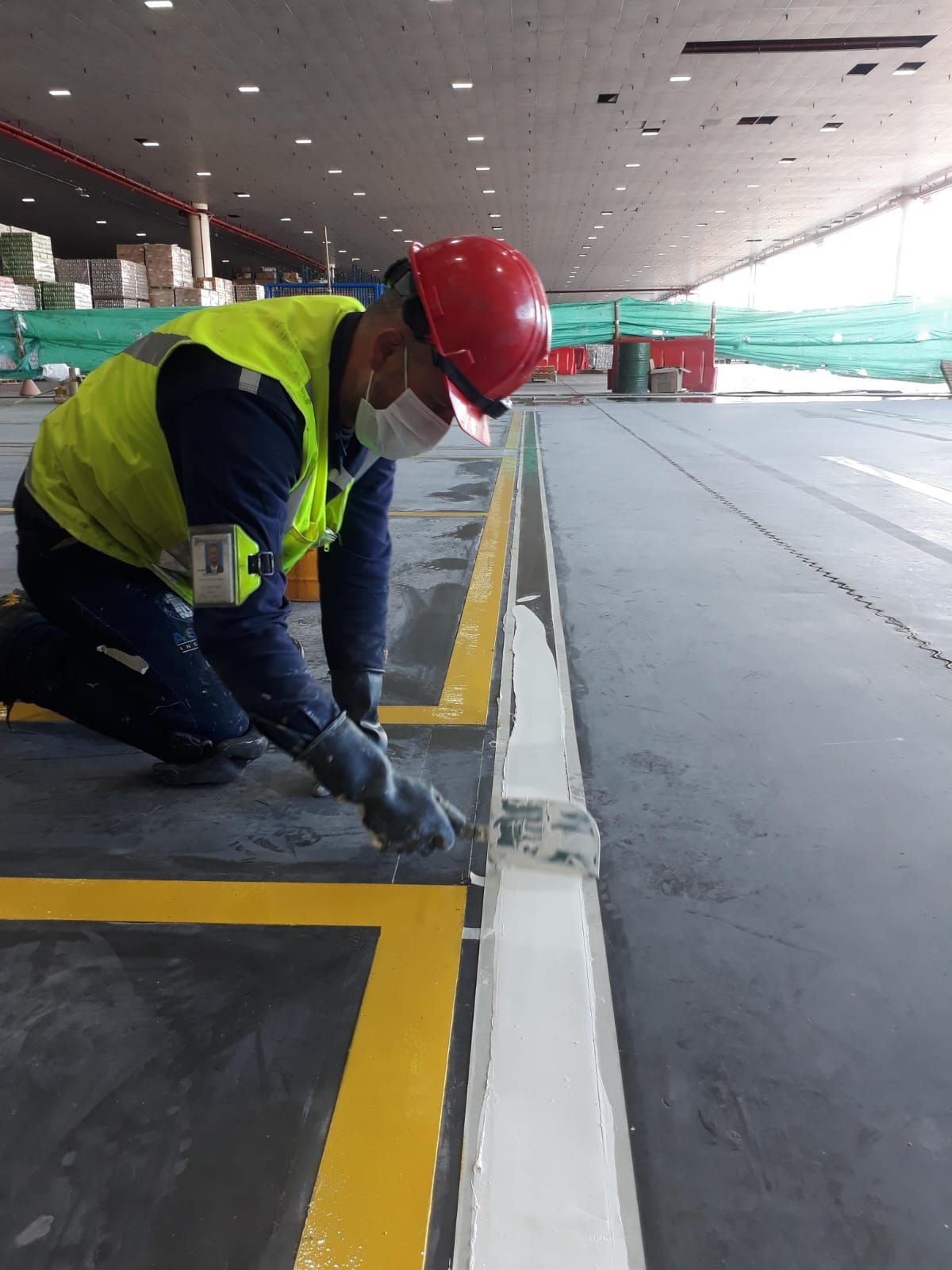 Persona con equipo de seguridad pintando una línea blanca sobre un suelo gris en un espacio abierto piso epóxico