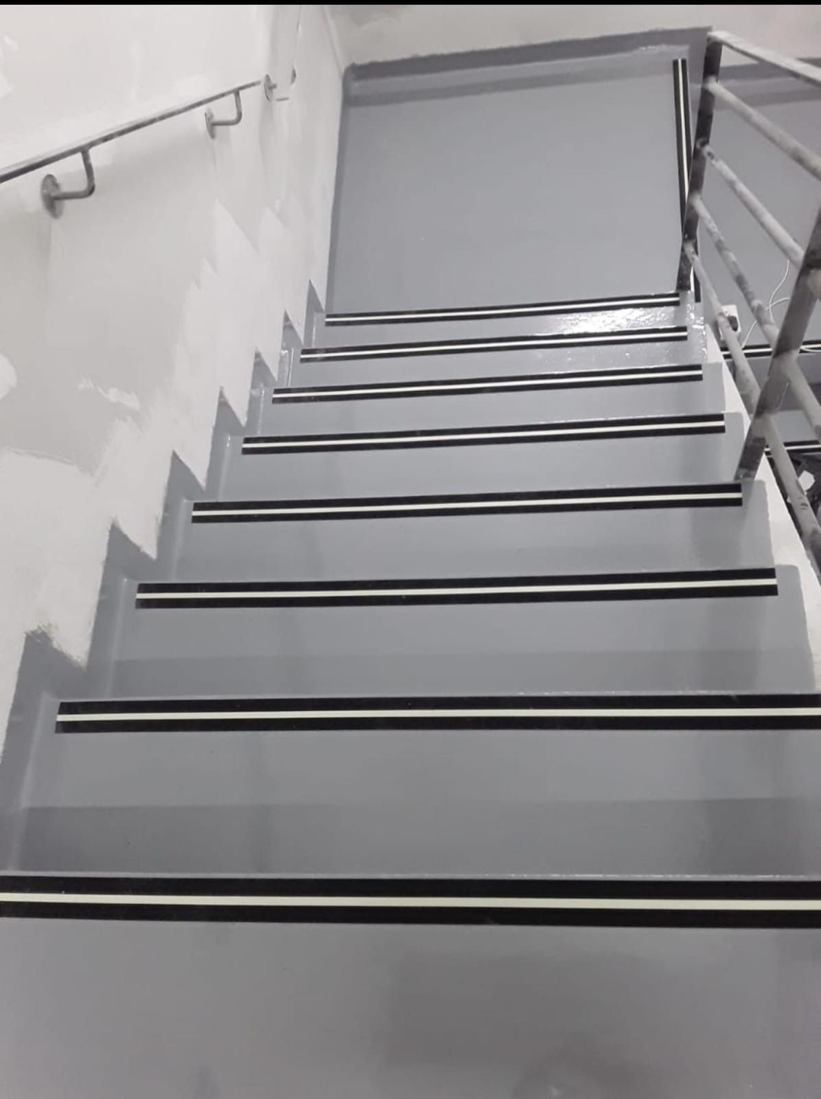 Escalera gris con rayas blancas y negras en los escalones, barandilla a derecha e izquierda.