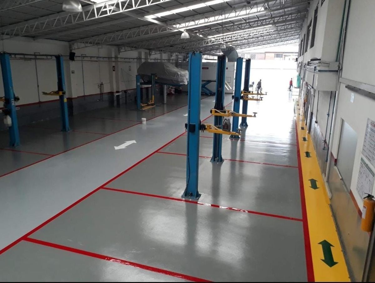 Taller mecánico vacío con suelo gris, marcas rojas y amarillas y elevadores de vehículos azules.