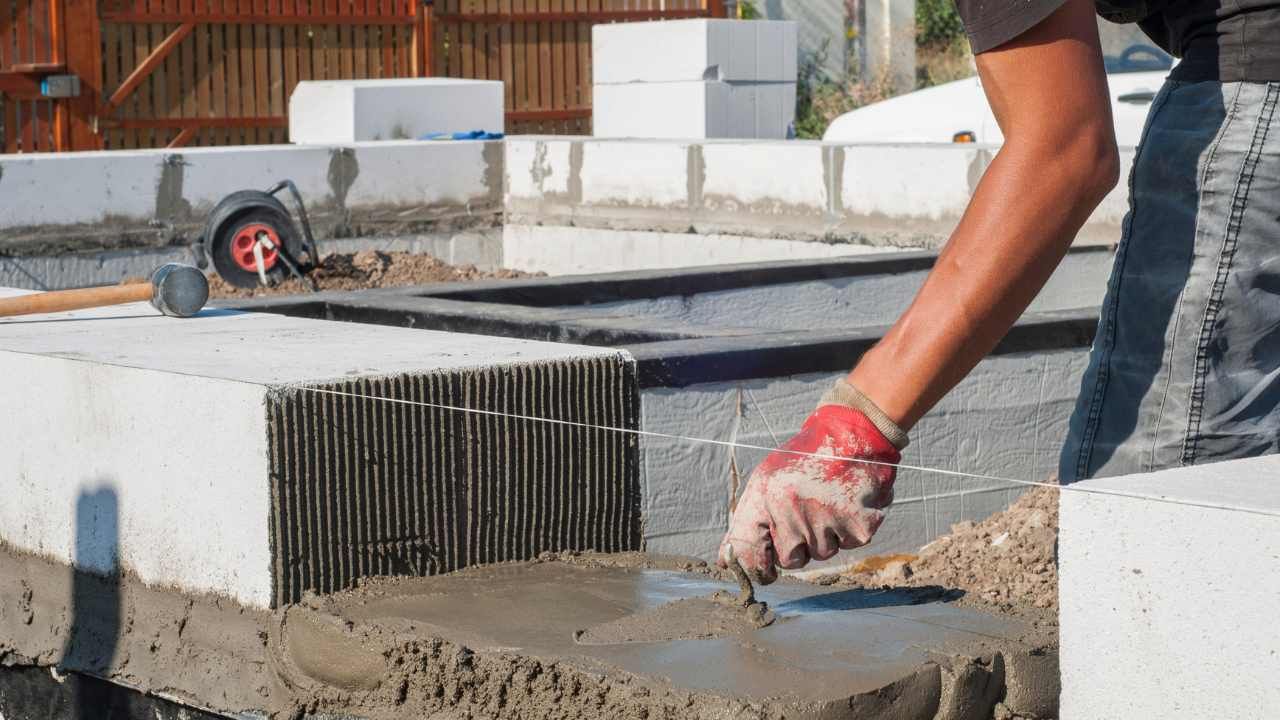 Close-up of mortar being applied along a concrete block wall during block and retaining wall work