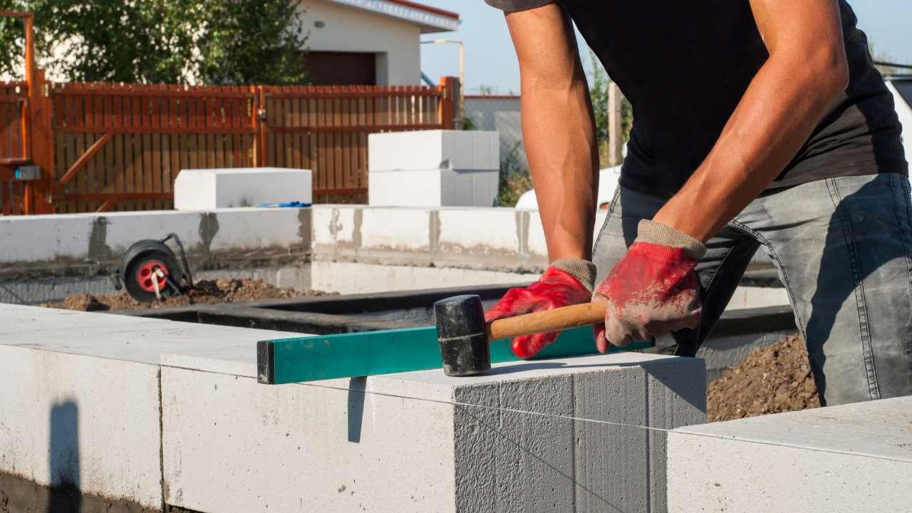 “Worker spreading mortar across the top of a block wall with rebar during block and retaining wall installation”