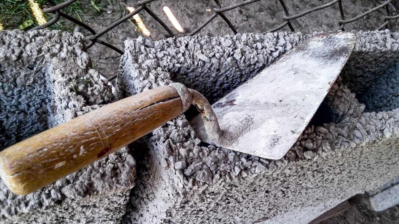 Close-up of a trowel moving wet mortar for block and retaining wall construction