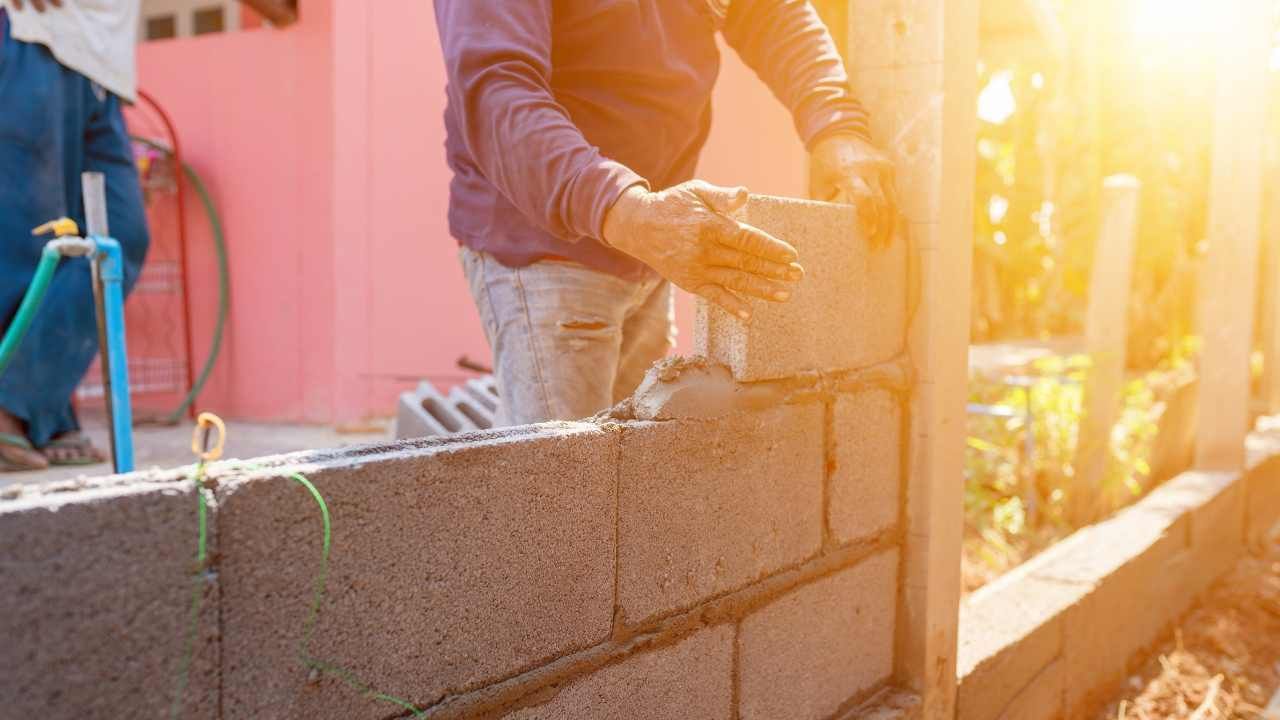 Worker laying concrete blocks in warm sunlight during block and retaining wall construction