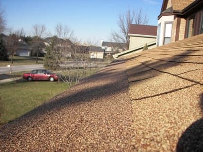 Roof covered with tan granular material beside a red car and houses on a sunny day
