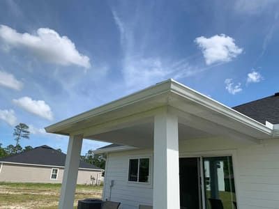 White house exterior with a covered patio, sliding glass door, and blue sky overhead