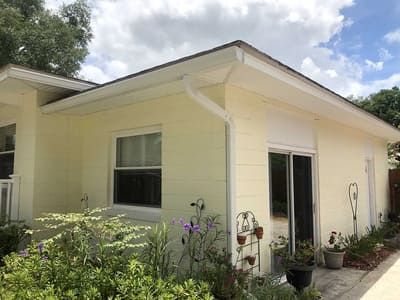 Small yellow house with white trim, sliding glass door, and potted plants along the patio.