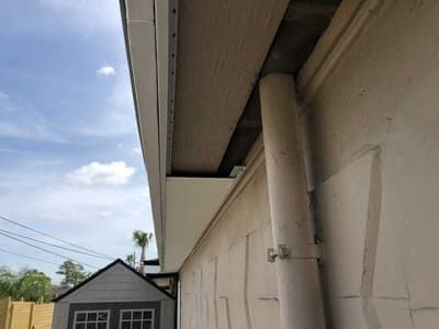 Side of a beige building with a roof overhang, a small gray shed, and blue sky with clouds.
