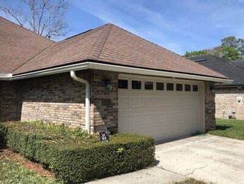 Suburban brick house with a tan garage door, trimmed hedges, and a driveway under a clear sky