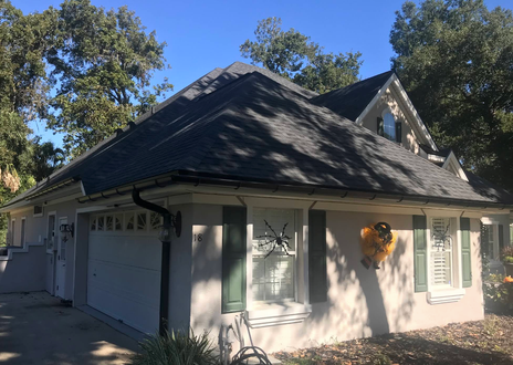 White house with dark roof and green shutters, shown from the front under trees on a sunny day