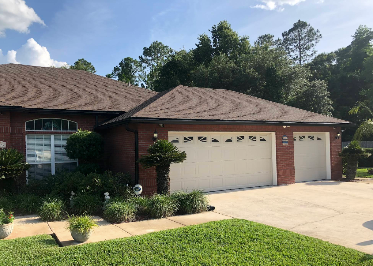 Brick suburban house with two-car garage, front lawn, and trees under a sunny sky