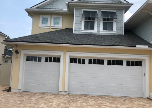 Two-story beige house with double white garage doors and a brick driveway