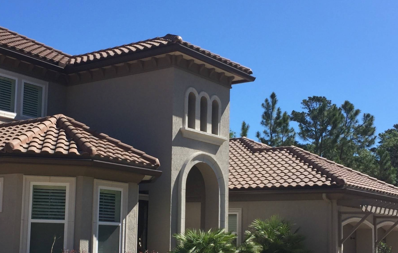 Stucco house with terracotta tile roofs and arched windows under a clear blue sky