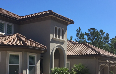 Stucco house with terracotta tile roofs and arched windows under a clear blue sky