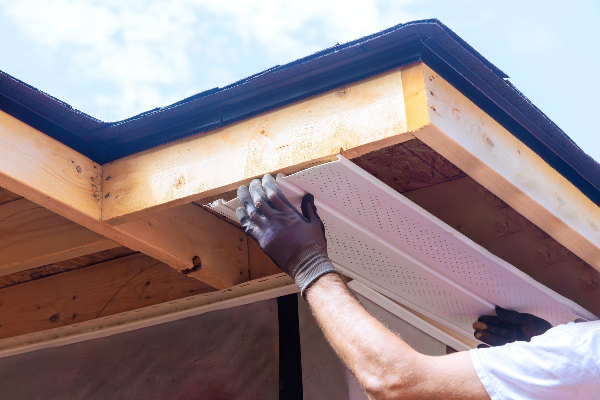 Worker installing soffit under a roof eave with hands and tools visible