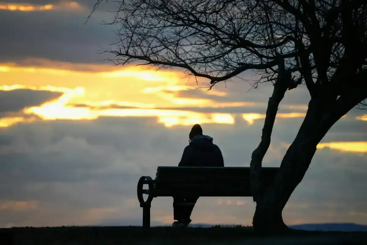 A man sits alone on a park bench at sunset.