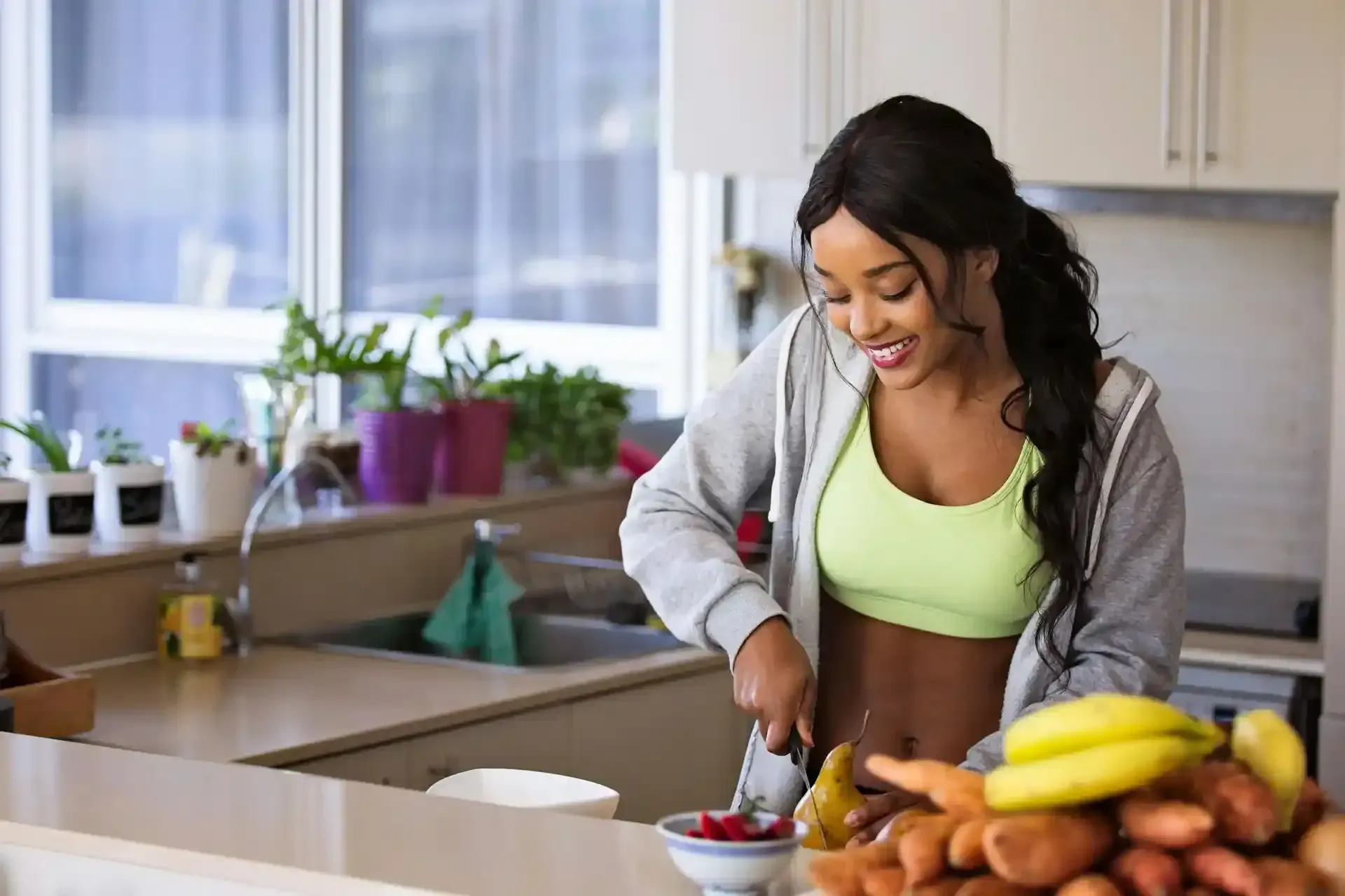 A woman cutting a pear and smiling at her kitchen counter