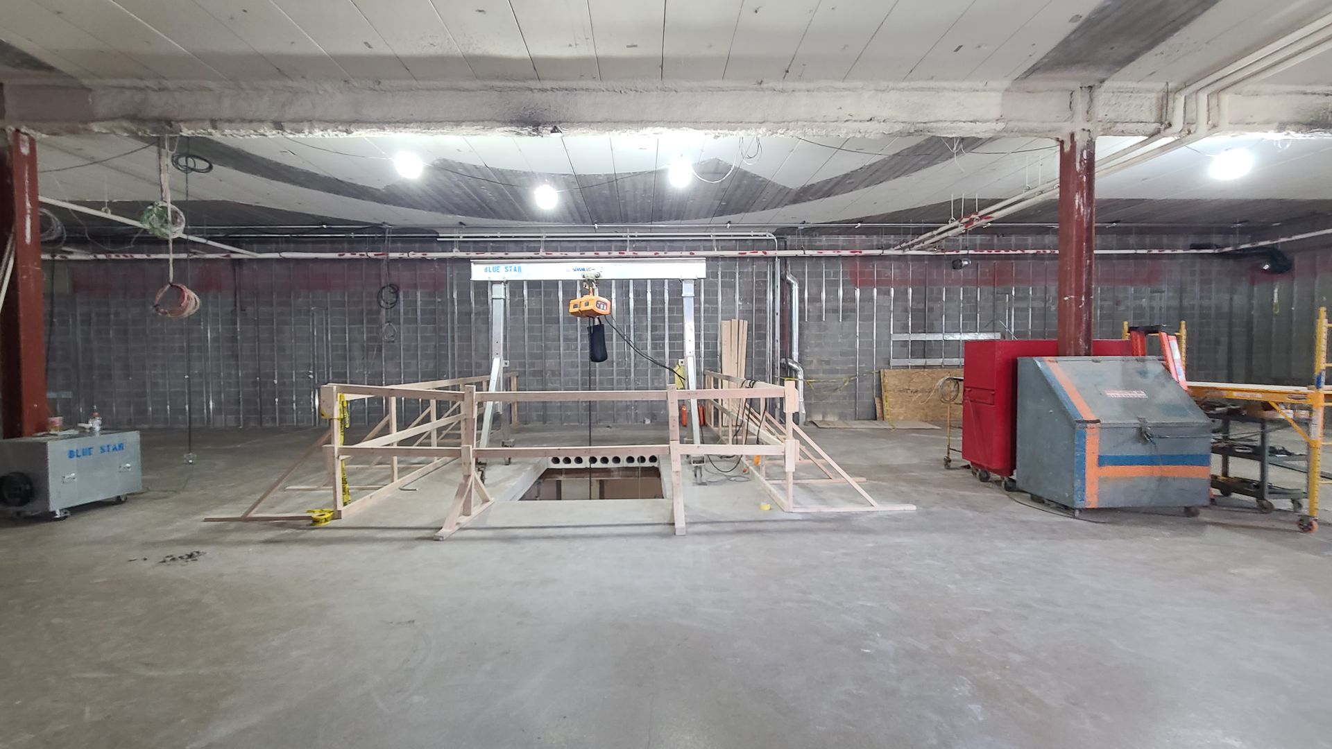 Construction site interior with scaffolding, tools, and exposed walls, ceiling, and concrete floor.
