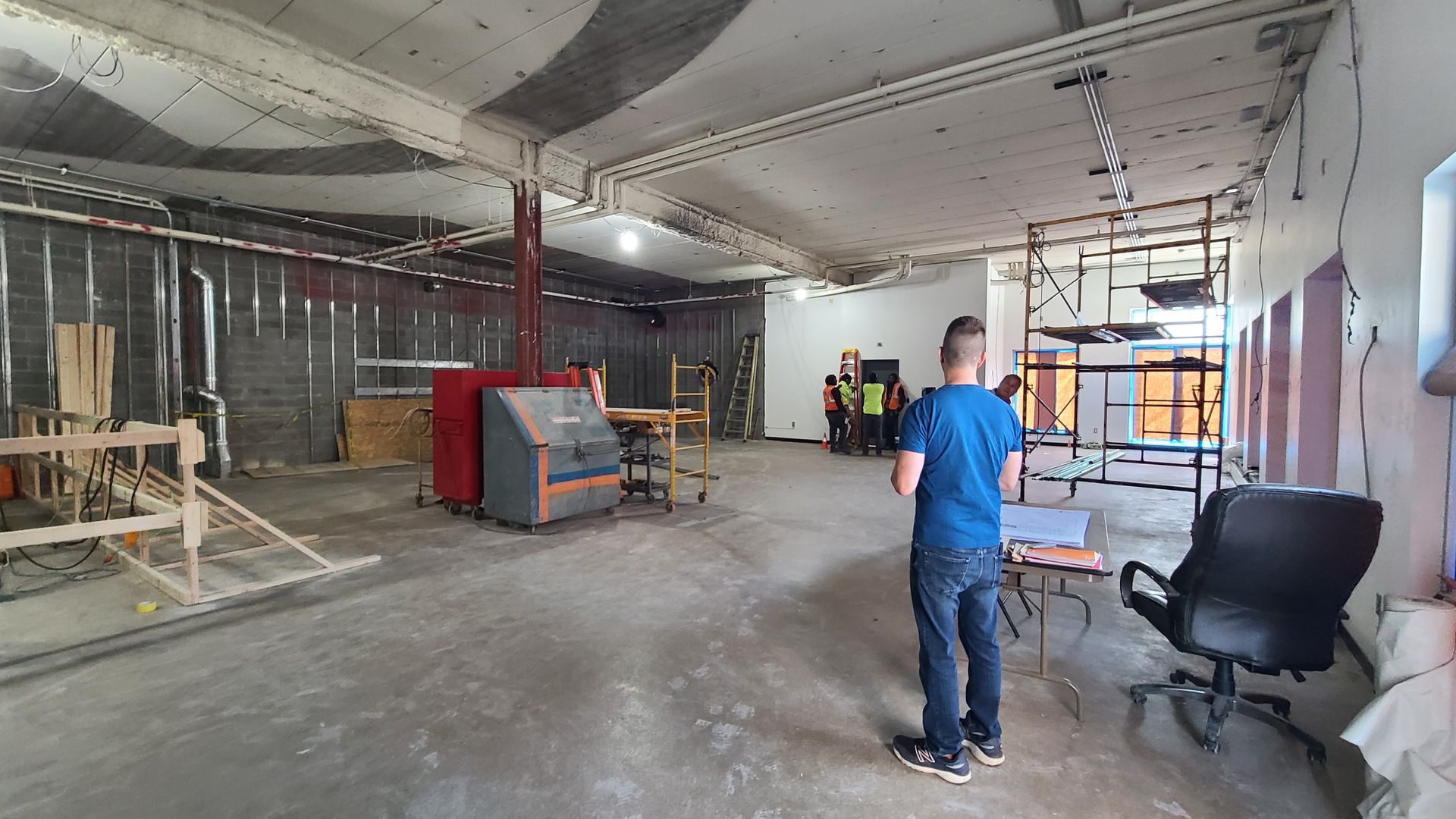A man stands in a construction zone, observing the open space, with tools and materials visible.
