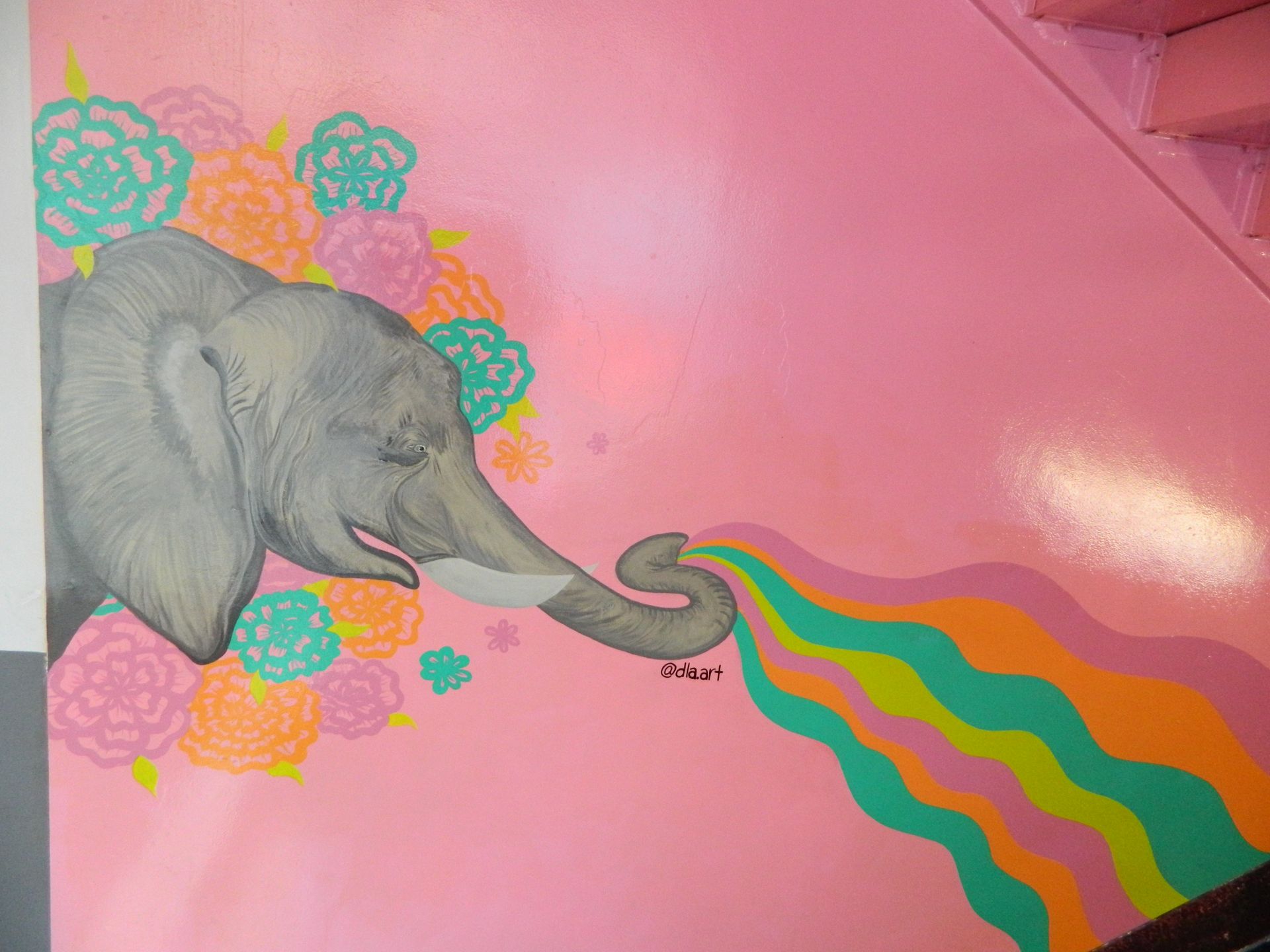 Pink wall mural: gray elephant spraying rainbow colors, surrounded by flowers.