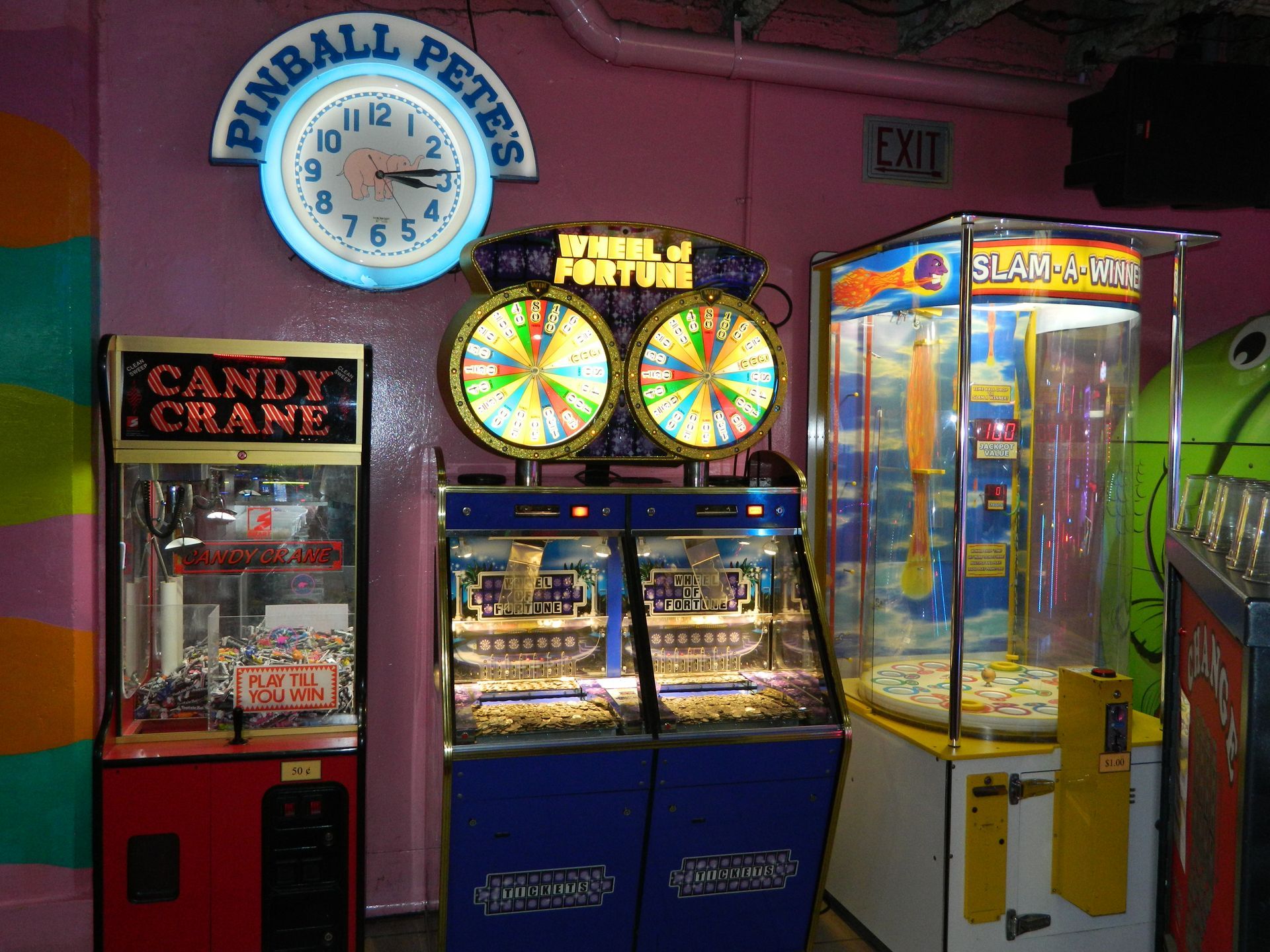 Arcade games: Candy Crane, Wheel of Fortune, and Slap-a-Ham.  Pink walls, clock sign, EXIT sign.