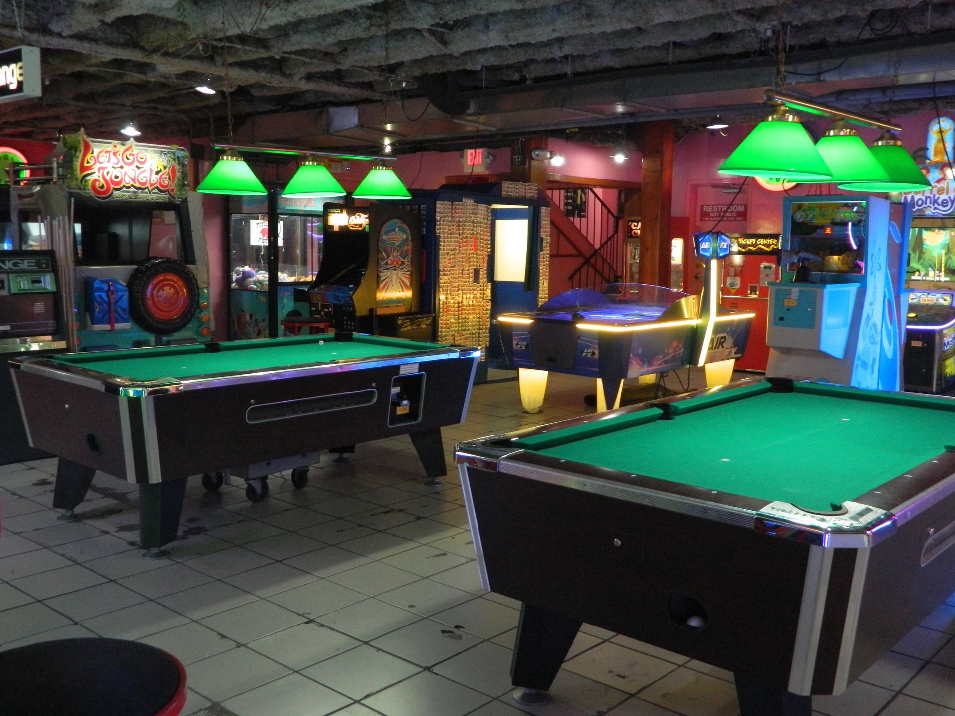 Interior of a dimly lit arcade with pool tables and various game machines.