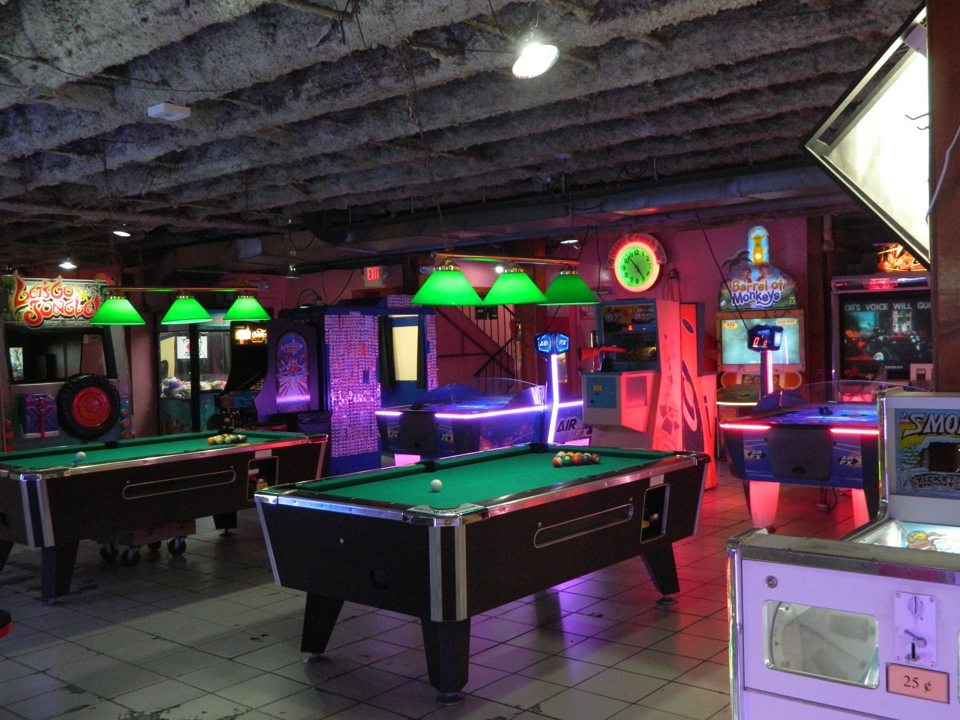 An arcade and pool hall. Dimly lit with pool tables, arcade games, and neon lights.